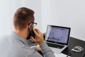 Businessman analyzing stock market data on a laptop while talking on the phone at his desk.