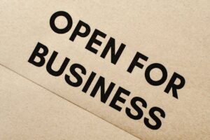 Close-up of an 'Open for Business' sign on a textured brown paper background.